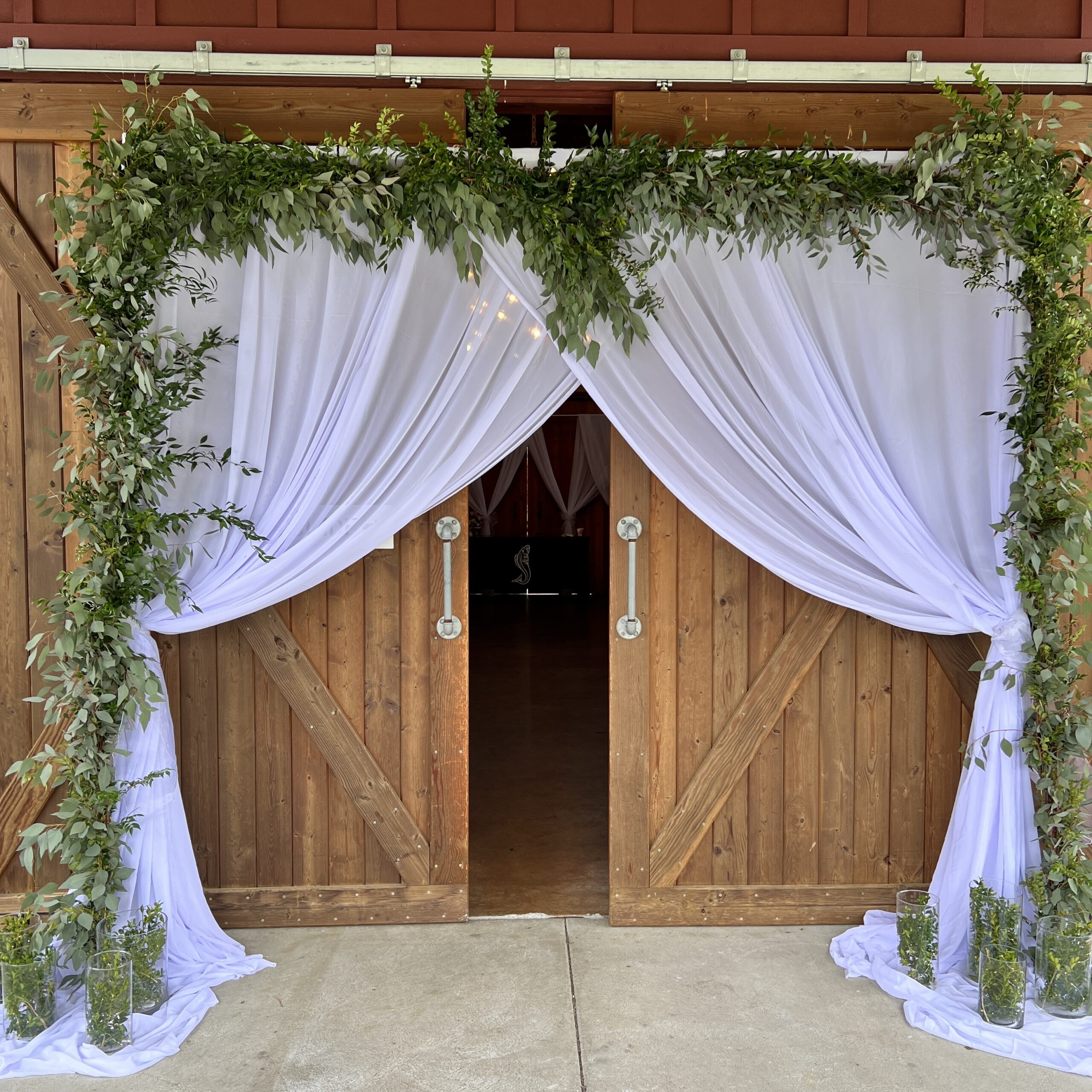 Rustic wooden doors with white drapes and greenery.